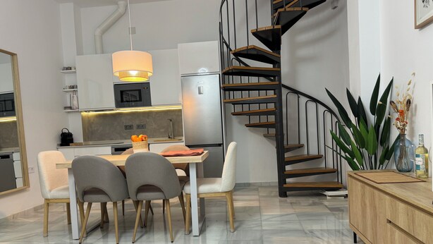 Una cocina moderna con comedor, una escalera de caracol y una planta grande.