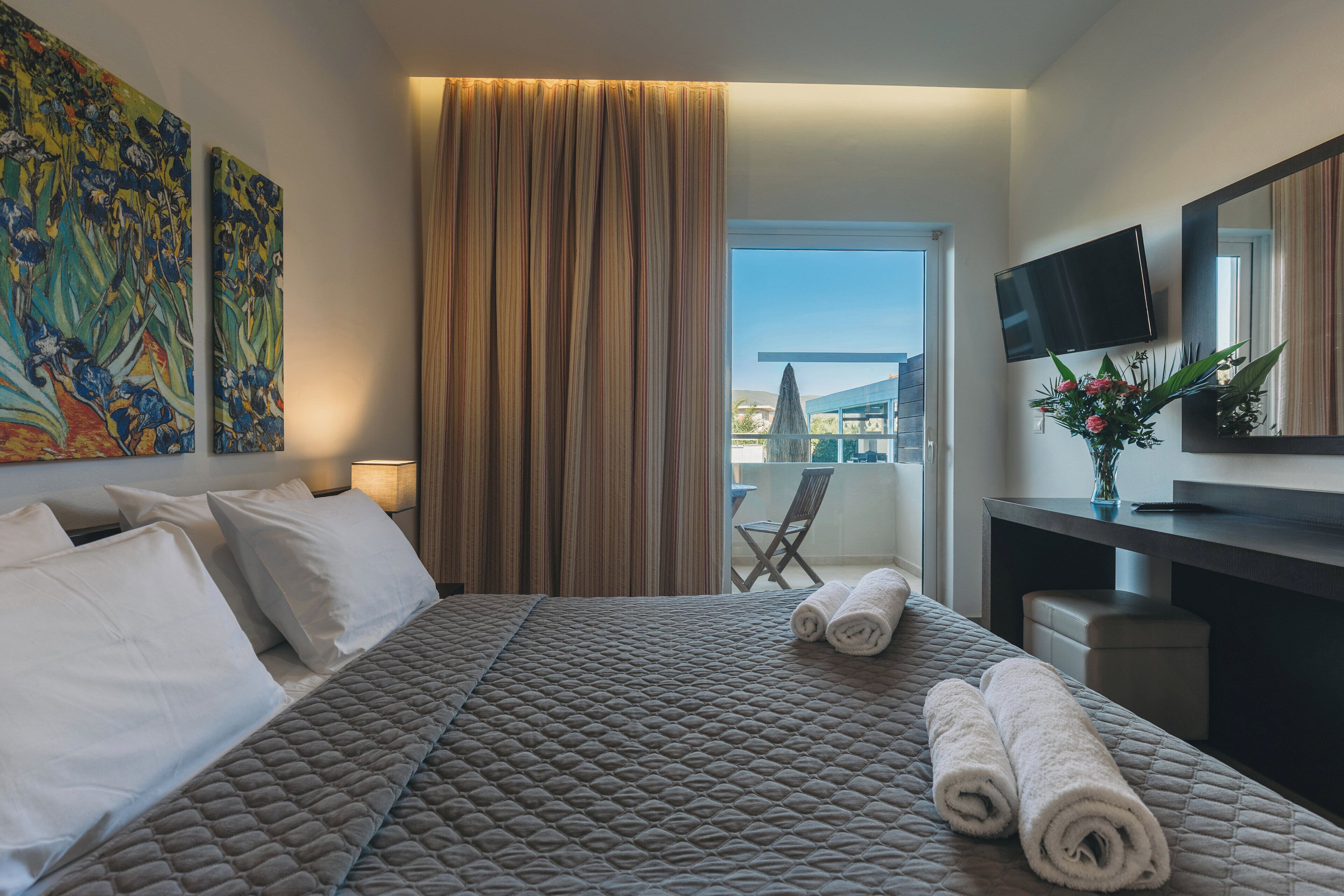 Habitación de hotel con cama, escritorio, televisor y balcón con una silla.