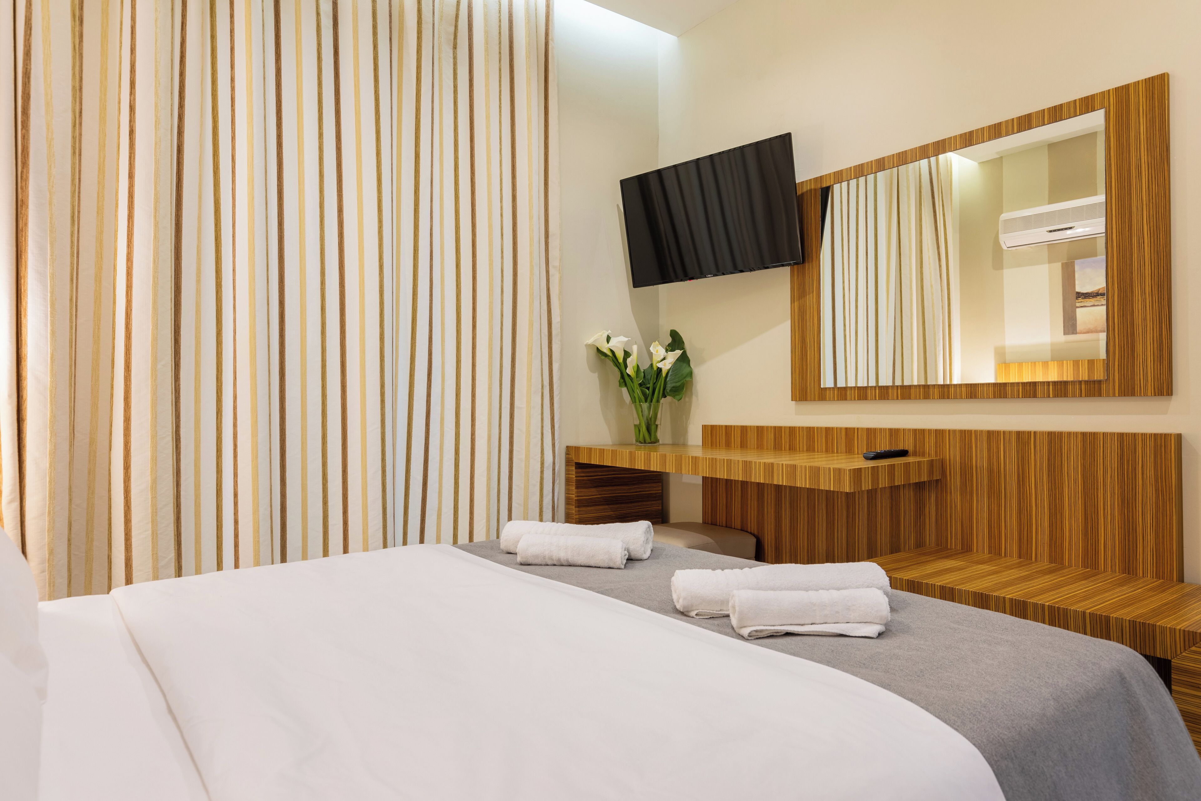 A modern hotel room with a large bed, a wooden vanity, a flat-screen TV, and a large mirror.