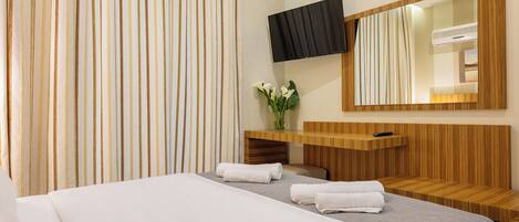 A modern hotel room with a large bed, a wooden vanity, a flat-screen TV, and a large mirror.