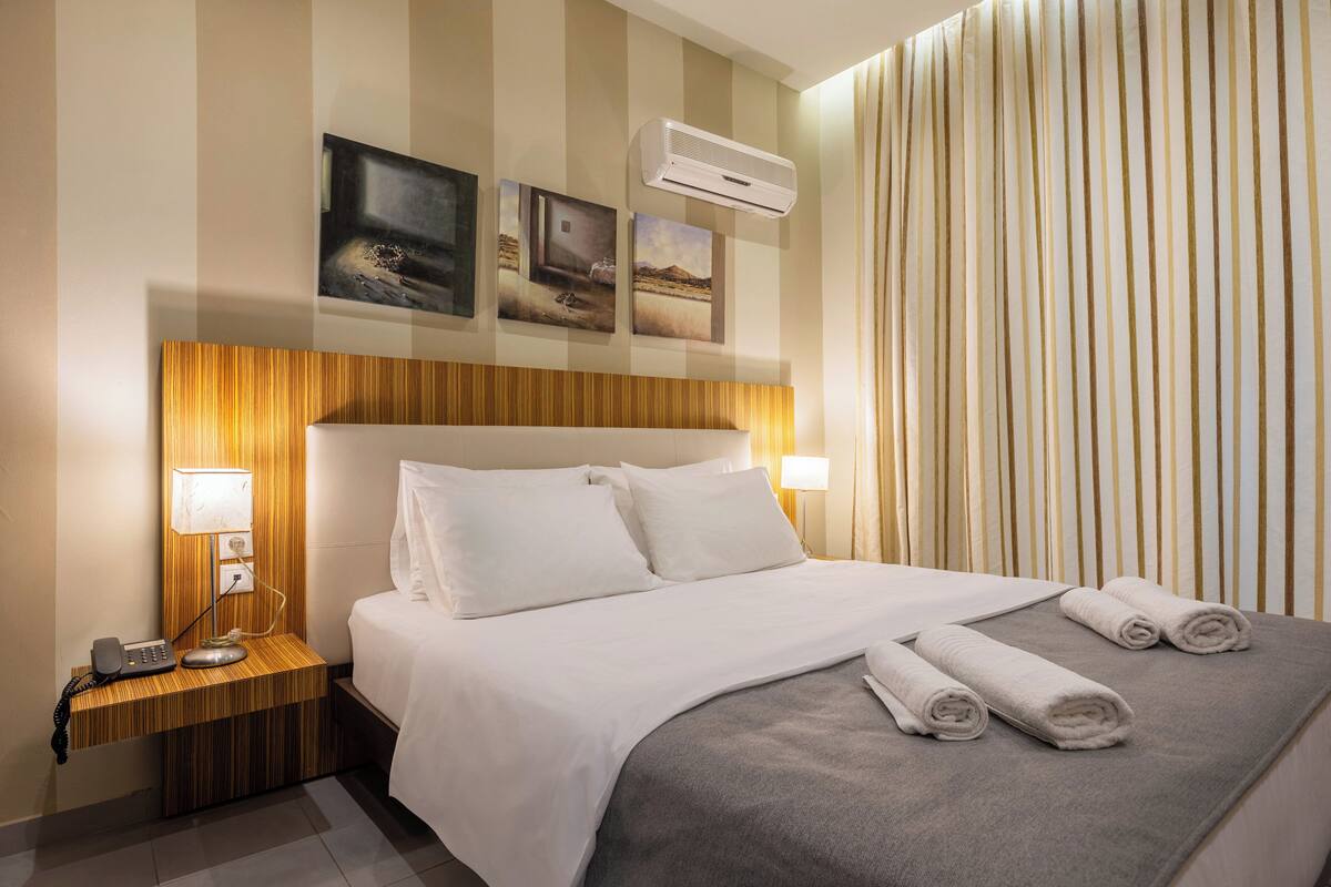 Hotelkamer met een groot bed, twee bedlampen, een telefoon en een luchtverkoeler aan de muur.