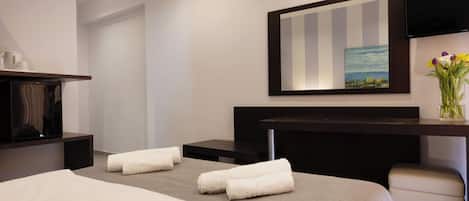 A hotel room with a bed, a desk with a flat-screen TV, a painting on the wall, and a vase with flowers.