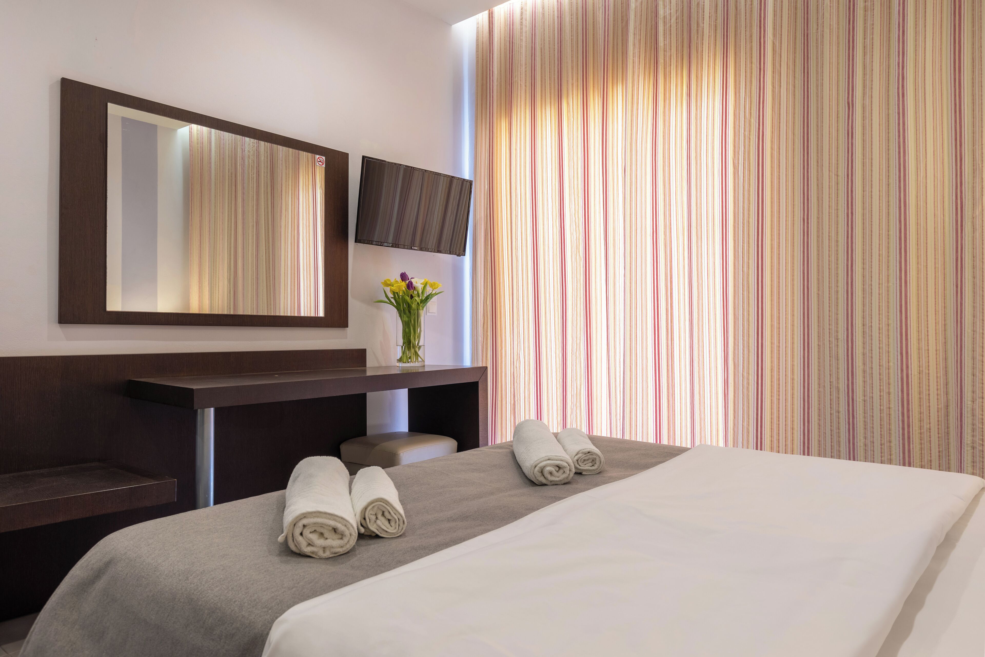 Une chambre d’hôtel équipée d’un lit, d’un bureau, d’une chaise, d’un téléviseur à écran plat et d’une fenêtre avec des rideaux à rayures.