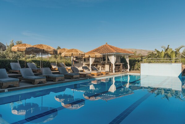 Un área de piscina con sillas de descanso, un bar y sombrillas de paja.