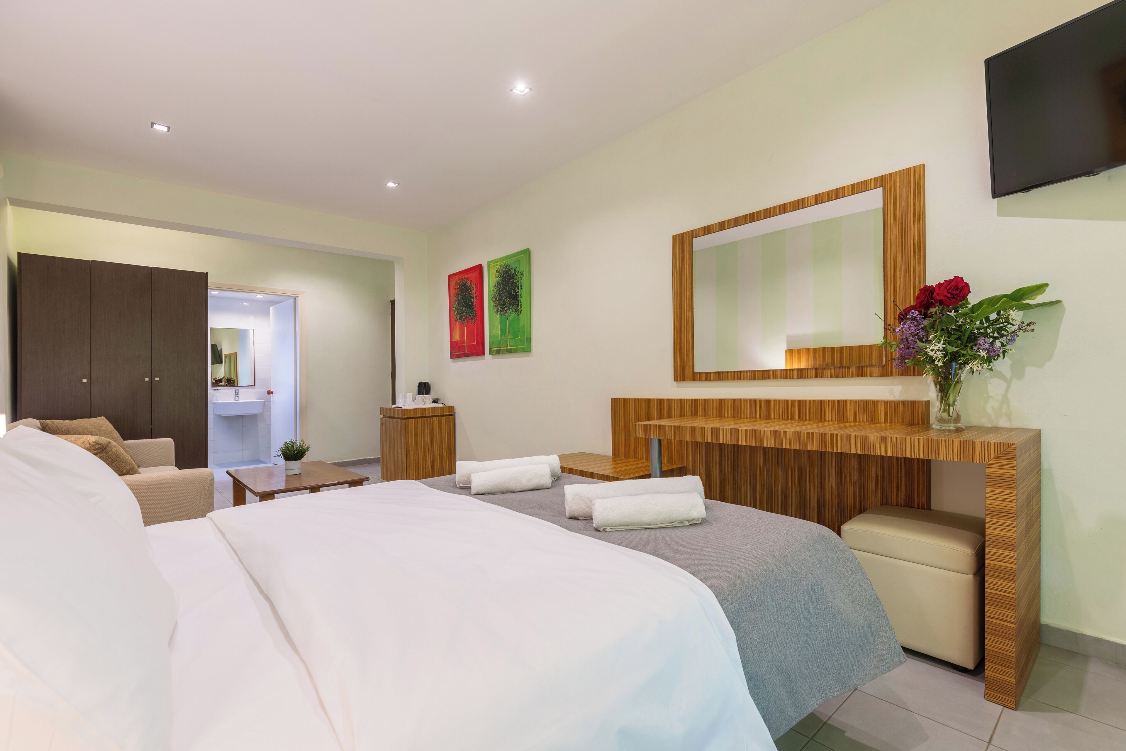 Een moderne hotelkamer met een groot bed, een houten kaptafel, een spiegel en een televisie aan de muur.