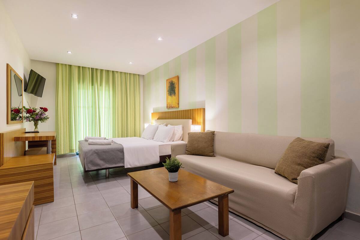 Een hotelkamer met een bed, een bank, een houten bijzettafeltje, een bureau en een spiegel.