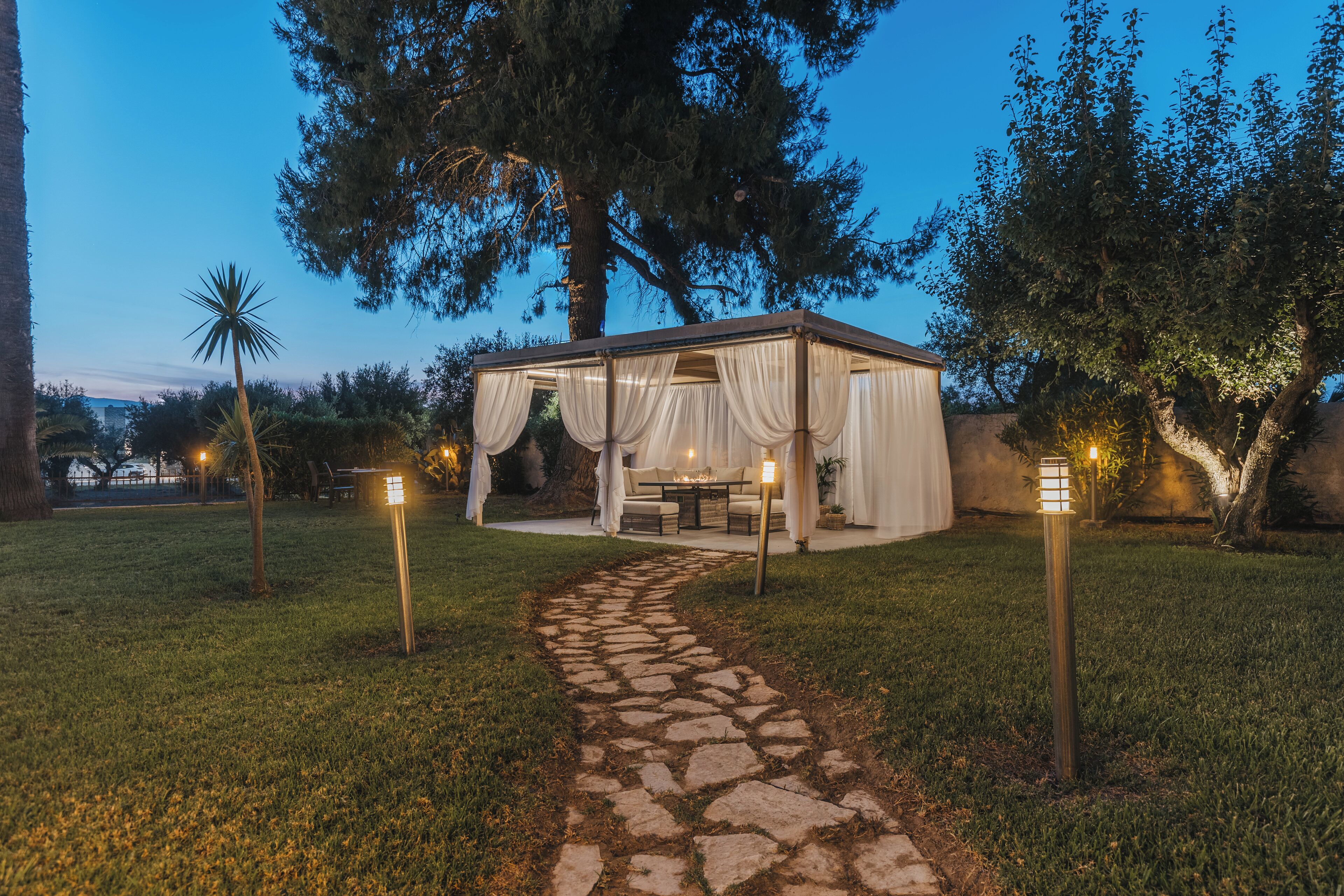 Un gazebo con un vialetto in pietra che vi conduce, circondato da alberi e illuminazione esterna.