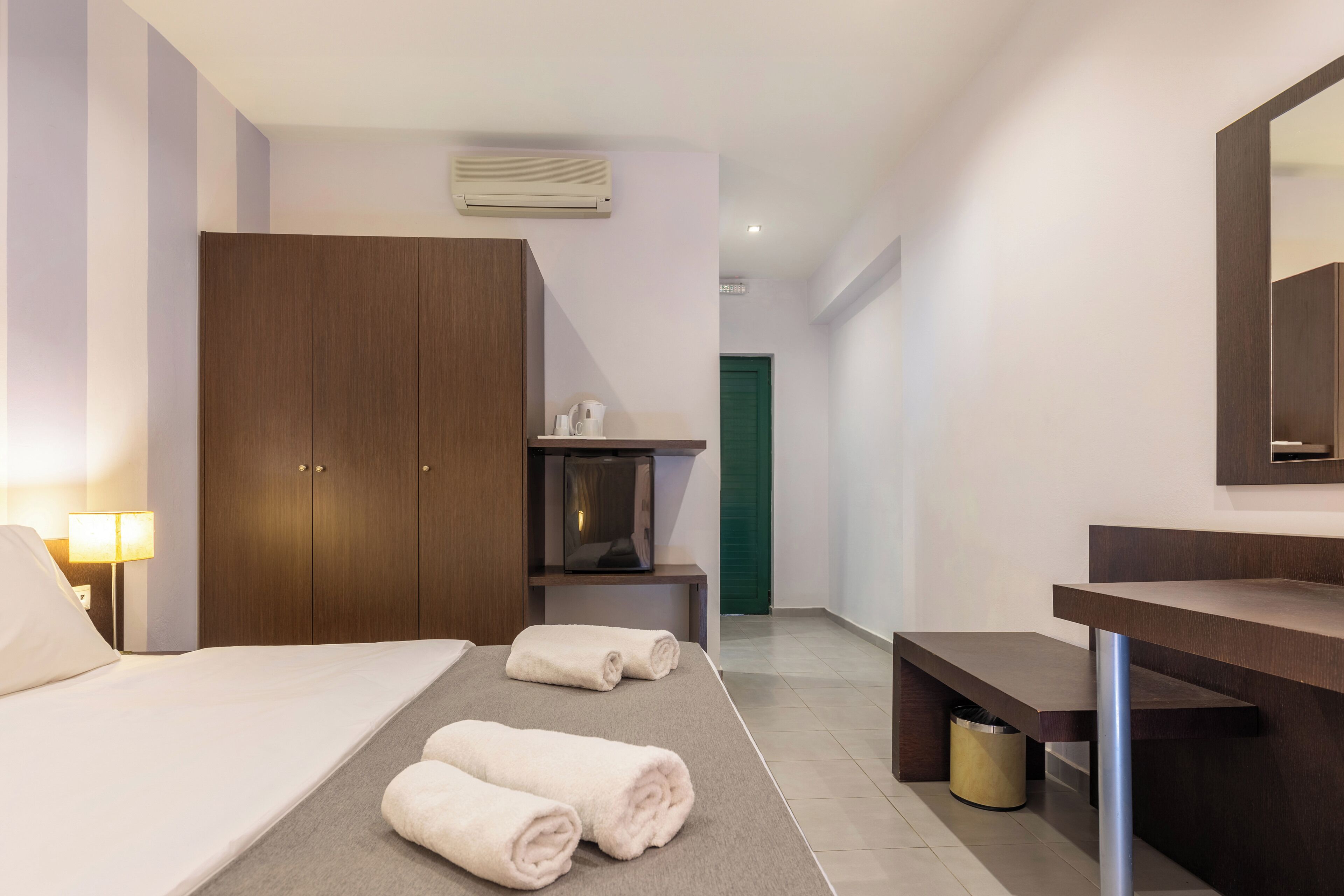 Une chambre d’hôtel avec un lit, deux serviettes enroulées, une télévision, un bureau, un miroir et une poubelle.
