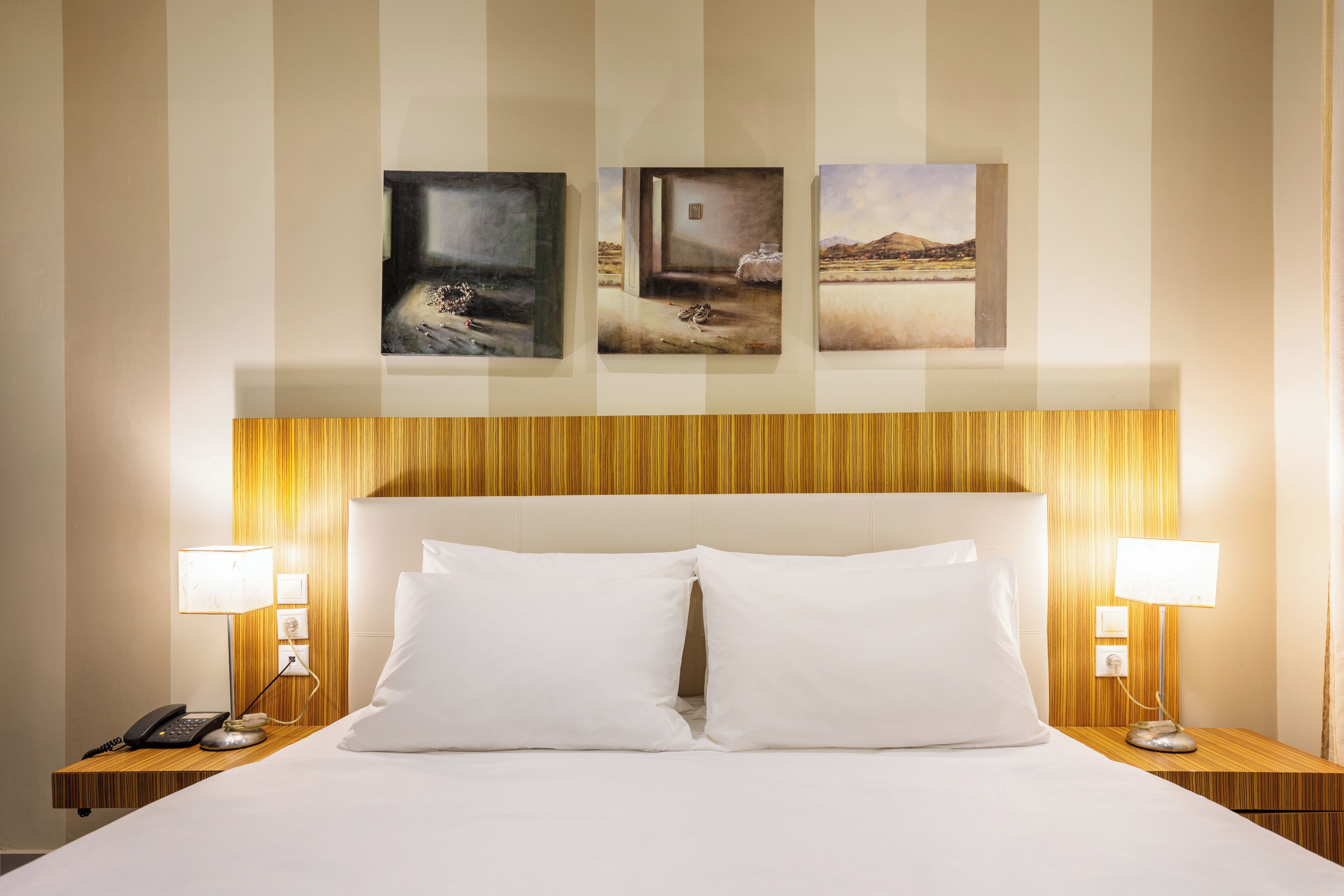 A hotel room with a large bed, two bedside tables with lamps, and three framed pictures on the wall.