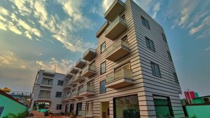 Un edificio moderno de varios pisos con balcones, una entrada central y un camino alfombrado de rojo que lleva a la entrada.