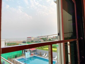 A view of a swimming pool with lounge chairs, a covered area, and a building in the background. - The Triton Beach Resort (Kanthi)