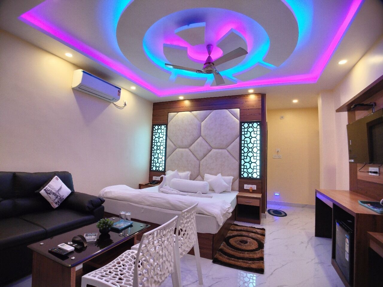 A modern hotel room with a bed, a sofa, a coffee table, a TV, and a ceiling fan.