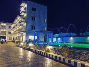 Um hotel com vários andares, piscina e fonte.