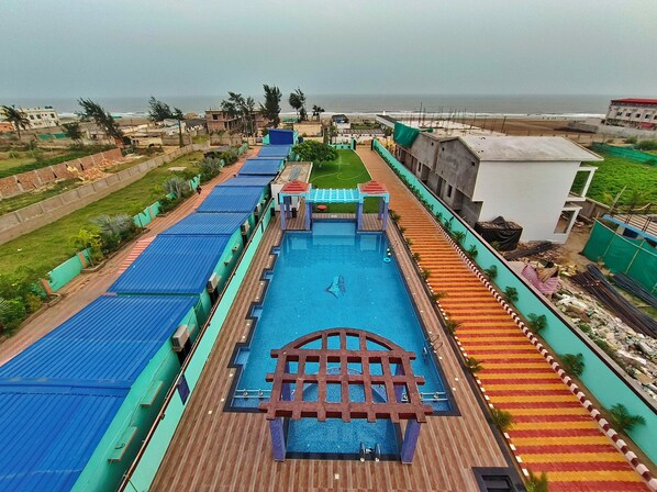 A swimming pool with a wooden deck, surrounded by a green fence and a colorful tiled walkway. - The Triton Beach Resort (Kanthi)