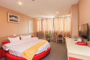 Habitación de hotel con cama, escritorio, silla, televisor y ventana con cortinas.