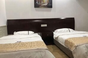 Ein Hotelzimmer mit zwei Betten, einem dunklen Kopfteil, einem Gemälde an der Wand und einem Heizkörper.