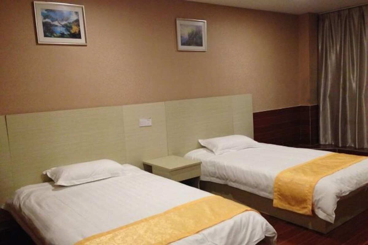 Two single beds with white linens and yellow accents, a headboard, and two framed pictures on the wall.