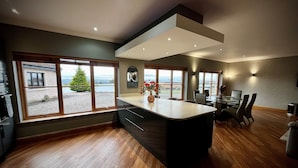 Una cucina moderna con una grande isola, pavimento in legno e ampie finestre che offrono vista sull'esterno.