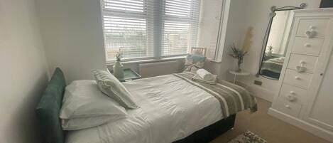A bedroom with a bed, bedside table, dresser, and a window with blinds.