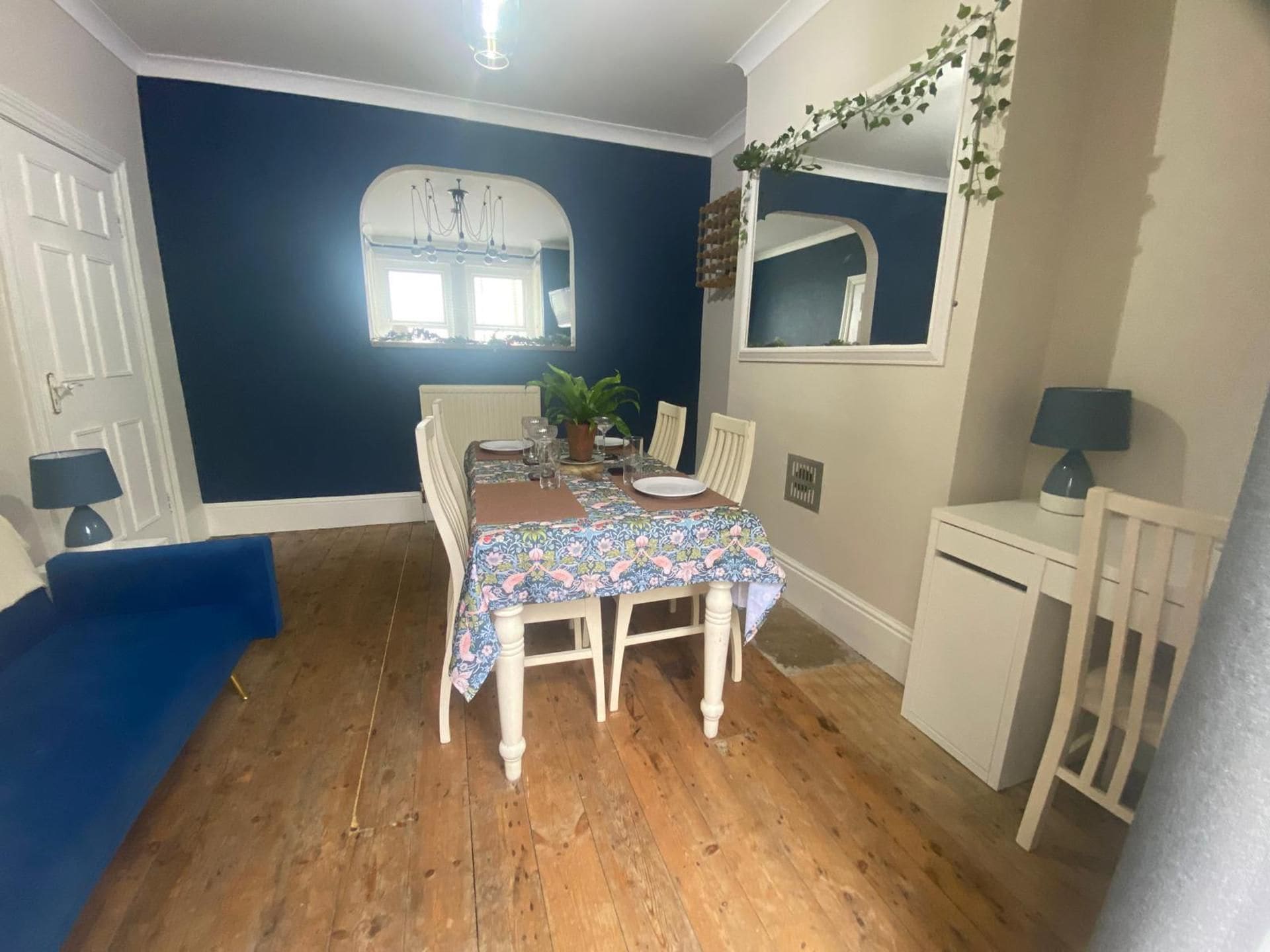 Un área de comedor con una mesa dispuesta para cuatro, un sofá azul y un mueble bajo.