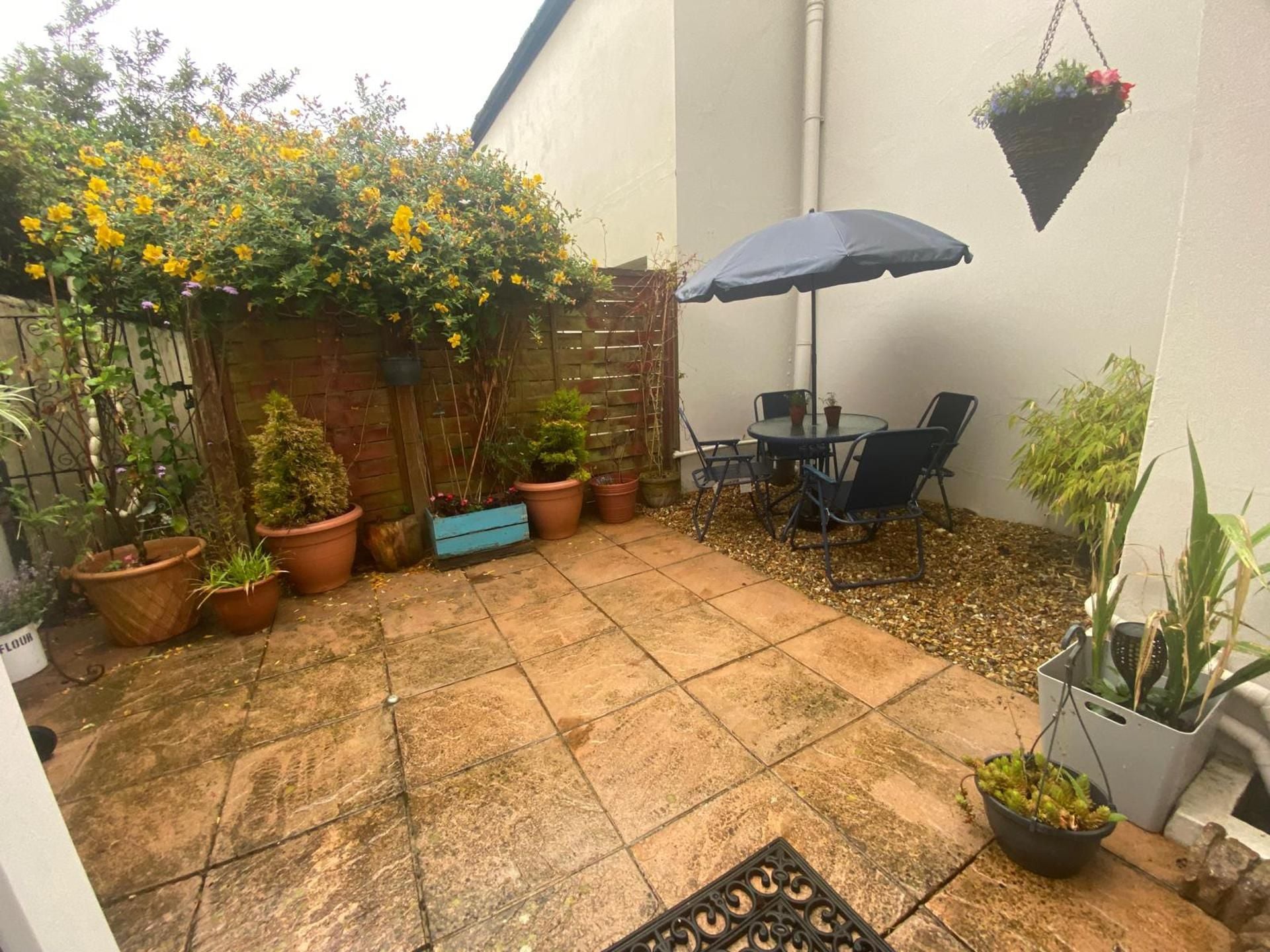 Un patio con mesa y sillas, plantas en macetas y una cesta de flores colgante.