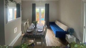 A dining area with a table set for four, a blue sofa, and a window with curtains. - Seaview 2 Bedroom House Sleeps 4 - Pets Ok -wifi (Shoreham-by-Sea)