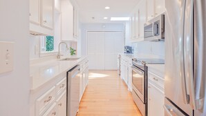 A modern kitchen with white cabinetry, stainless steel appliances, and a wooden floor. - Gorgeous Quiet Lakefront Beach Cottage Inside Wild Dunes! (Isle Of Palms)