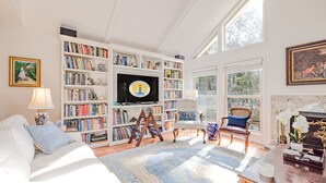 A well-lit room with a large bookshelf, a comfortable seating area, and a fireplace. - Gorgeous Quiet Lakefront Beach Cottage Inside Wild Dunes! (Isle Of Palms)
