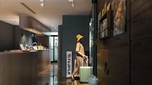 A modern hotel lobby with a reception desk, a Fujifilm sign, and a person with luggage. - June June House (Tainan)