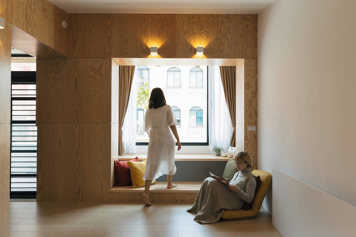 A room with a large window, a bench, and a person sitting on the bench.