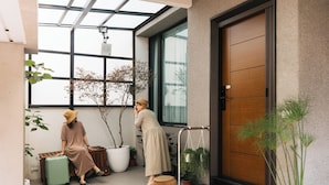 A modern interior with a large window, a wooden door, and potted plants. - June June House (Tainan)