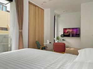A hotel room with a large bed, a desk with a chair, a TV on the wall, and a window with curtains. - June June House (Tainan)