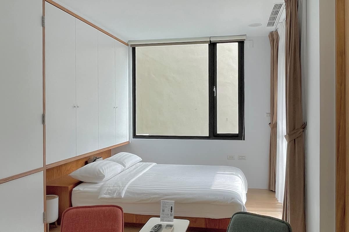 A bedroom with a bed, two chairs, a small table, and a window.