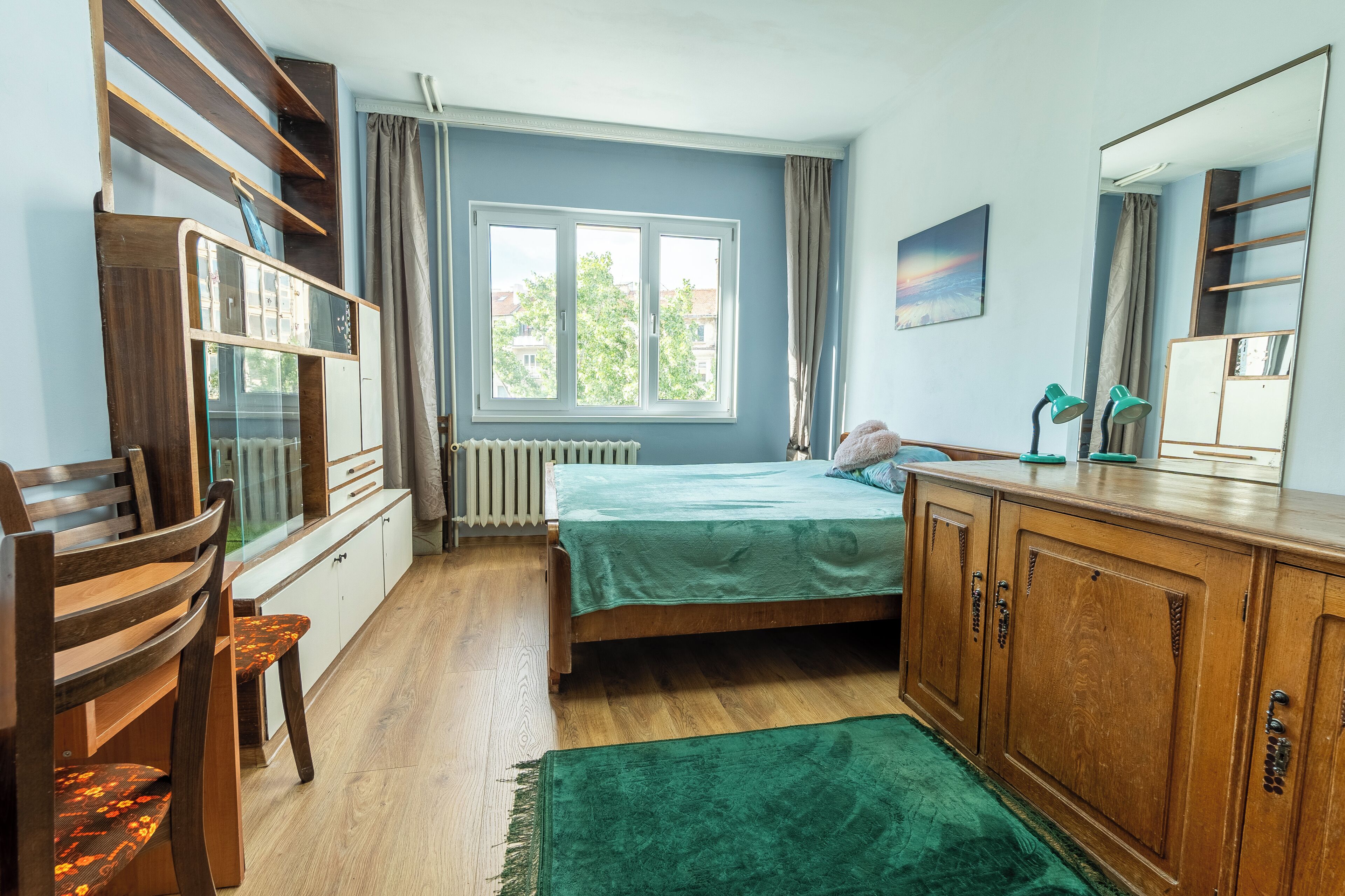 Een slaapkamer met een bed, houten meubels, een raam en een radiator.