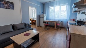 A compact living space with a sofa, a small dining table, a kitchenette, and a window providing natural light.