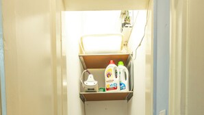 A compact laundry room with a washing machine and a shelf above containing cleaning supplies.