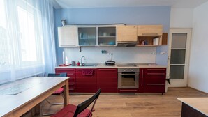 A modern kitchen with wooden cabinets, a red countertop, and a dining area with a wooden table and chairs.