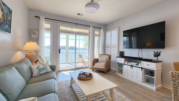 A living room with a sofa, a coffee table, a TV, and a view of the outdoors through large sliding doors. - Overlooking Saltwater Lake & near beach, 1 Minute to Pool! (Pawleys Island)