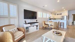 A modern living room with a sofa, dining table, and kitchen area with white cabinets and a flat-screen TV. - Overlooking Saltwater Lake & near beach, 1 Minute to Pool! (Pawleys Island)