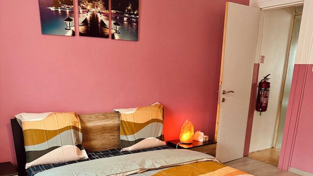 Quarto com cama, almofadas, mesa de cabeceira, aquecedor e porta com extintor de incêndio.