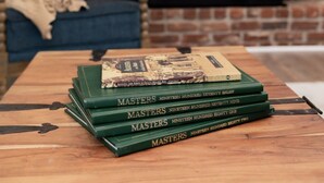 A stack of 'Masters' books on a wooden table in a room with a brick fireplace and a blue chair. - Spacious Woodbridge Cottage (Evans)