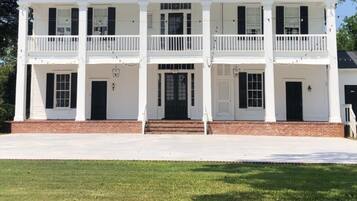A two-story white building with a central entrance, a balcony on the upper floor, and a brick foundation.