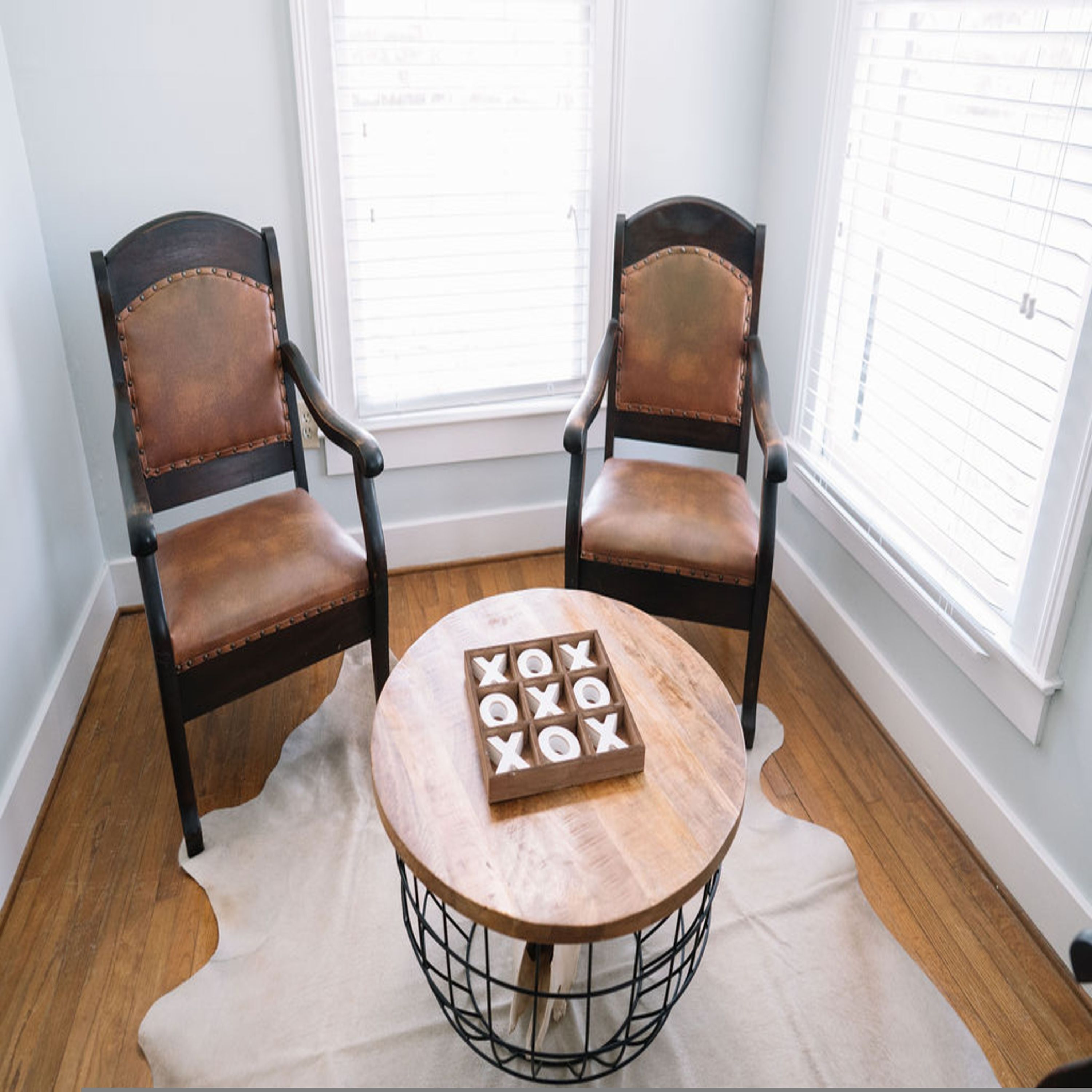 Two leather chairs with wooden frames and a round table with a woven base, placed on a rug.