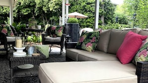 An outdoor seating area with wicker furniture, a cushioned sofa, and a table with decorative items. - Elegant Crofton Ranch (Augusta)