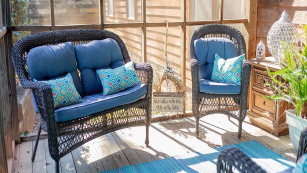 Une terrasse en bois agrémentée de meubles en osier, notamment d’un canapé et de fauteuils, ainsi que d’une lanterne décorative.