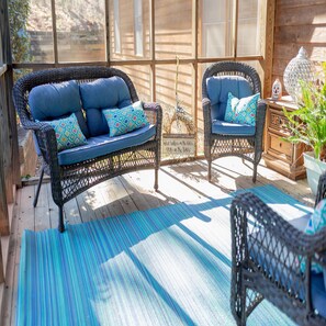 A wooden deck with wicker furniture, including a sofa and chairs, and a decorative lantern. - Autumn Woods Lodge (Grovetown)