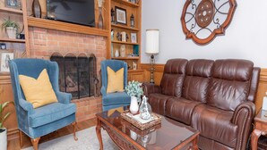 A living room with a brick fireplace, two blue armchairs, a brown leather sofa, and a wooden coffee table.