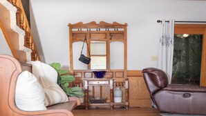 A wooden staircase, a wooden bench with cushions, a leather sofa, a wooden cabinet with a mirror, and a window with curtains.