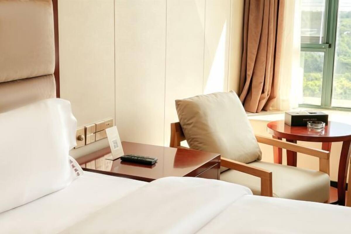 Hotellihuone, jossa on sänky, puinen työpöytä, tuoli ja ikkuna, jossa on verhot.