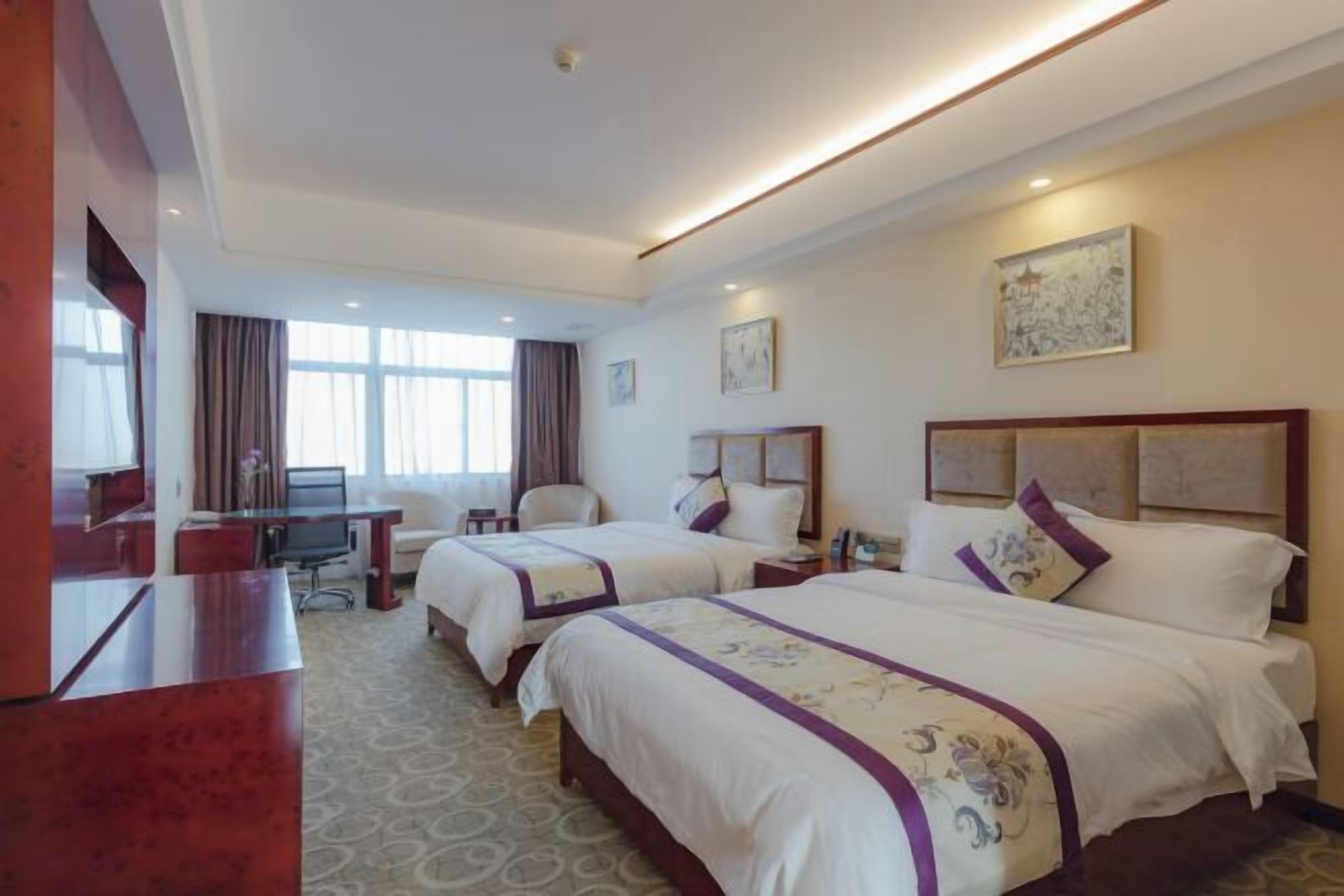 A hotel room with two beds, a desk, a chair, and a TV.